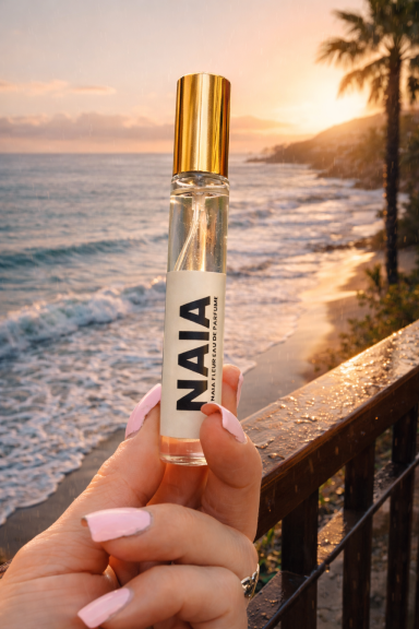 NAIA 10 ML Naia FLEUR NAIA perfume roller held near ocean at sunset, coastal inspired fragrance.
